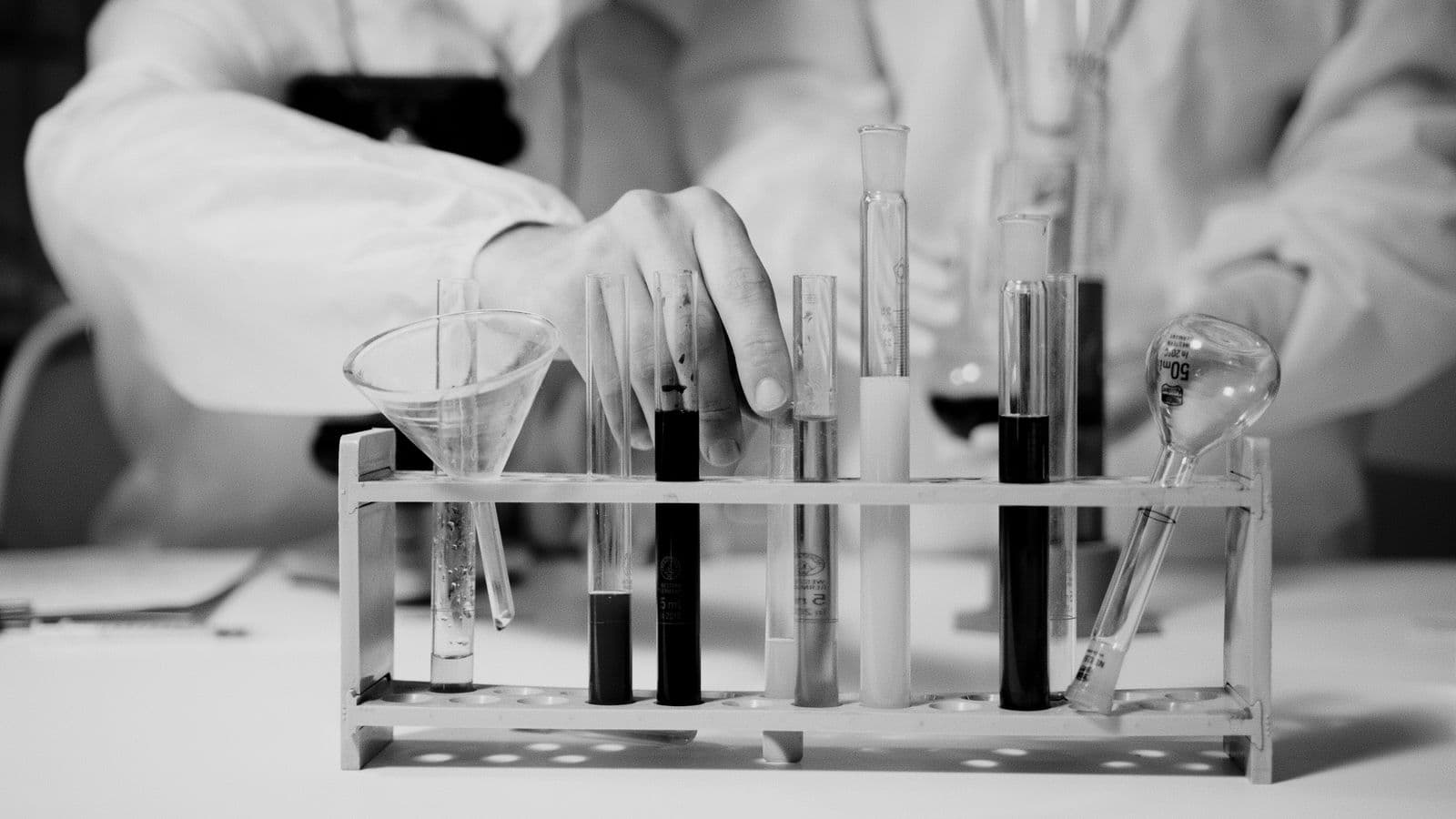A scientist's hand arranging test tubes in a rack, representing the careful reproduction work behind agent memory benchmarks